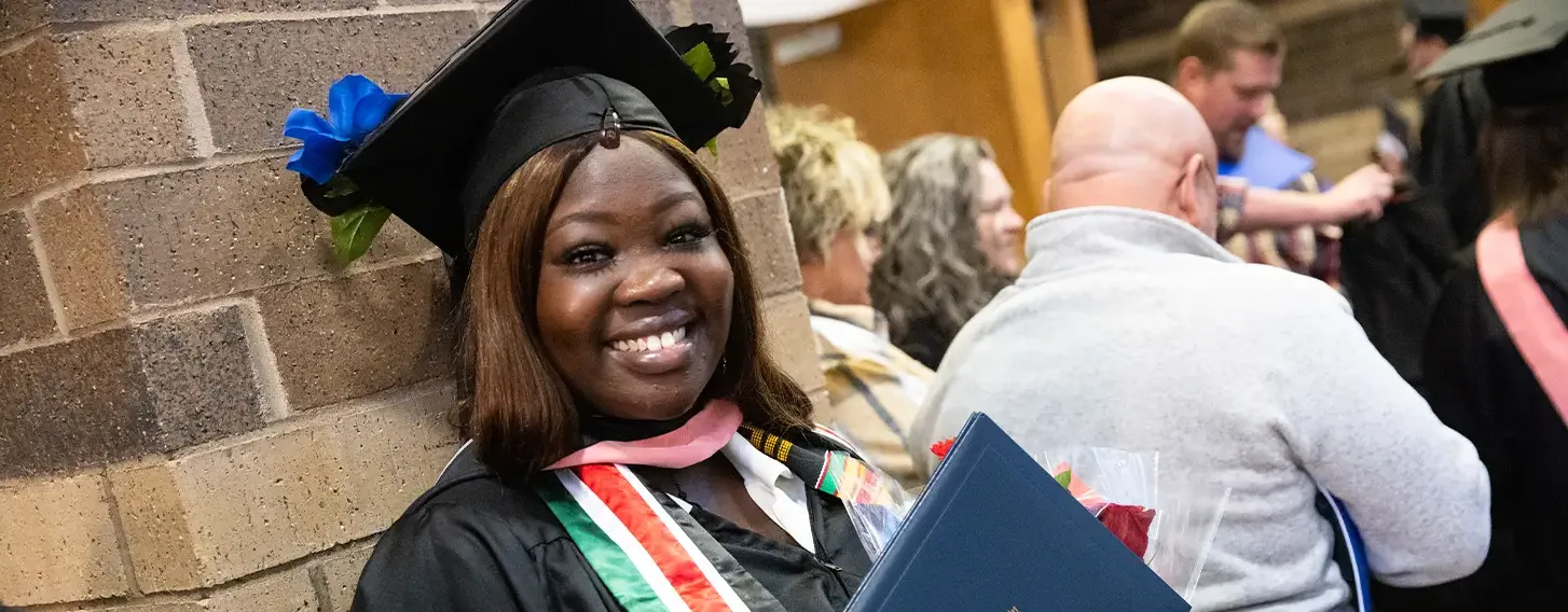 A graduate smiling, wearing a South Sudan flag stole at commencement